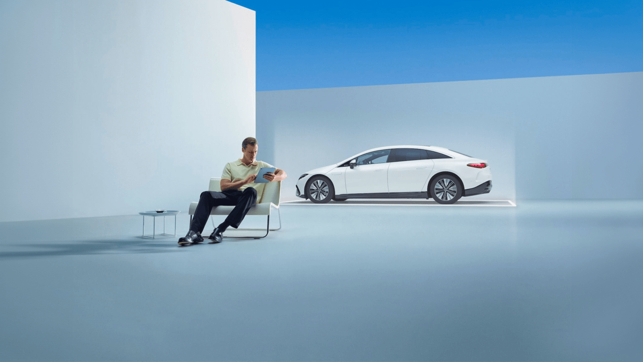 Homme assis regardant sa tablette avec son Mercedes EQE en arrière plan